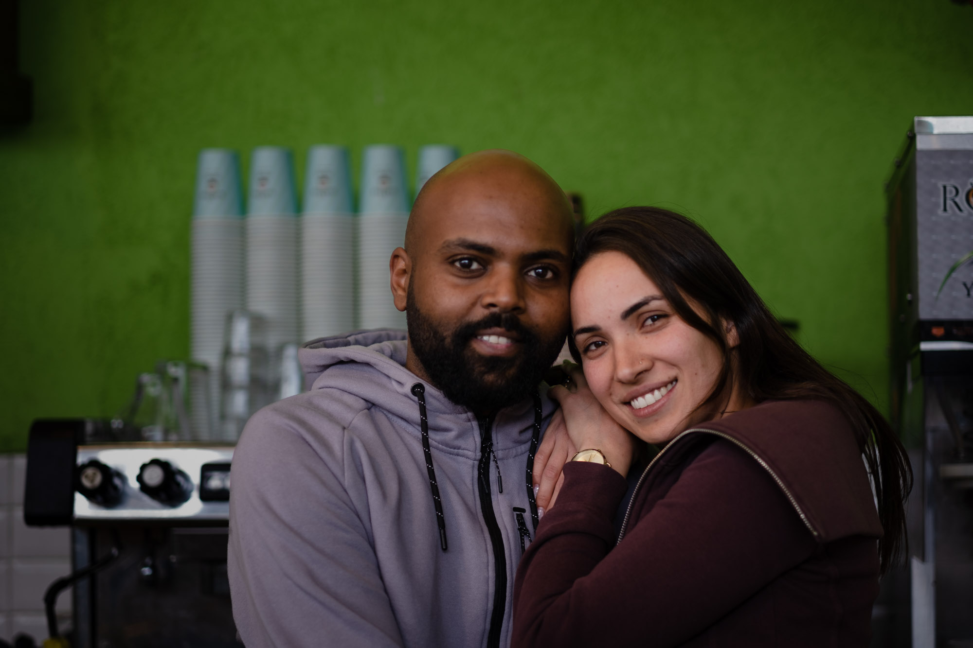 A couple sit close together and smile in a café with a vivid green wall.