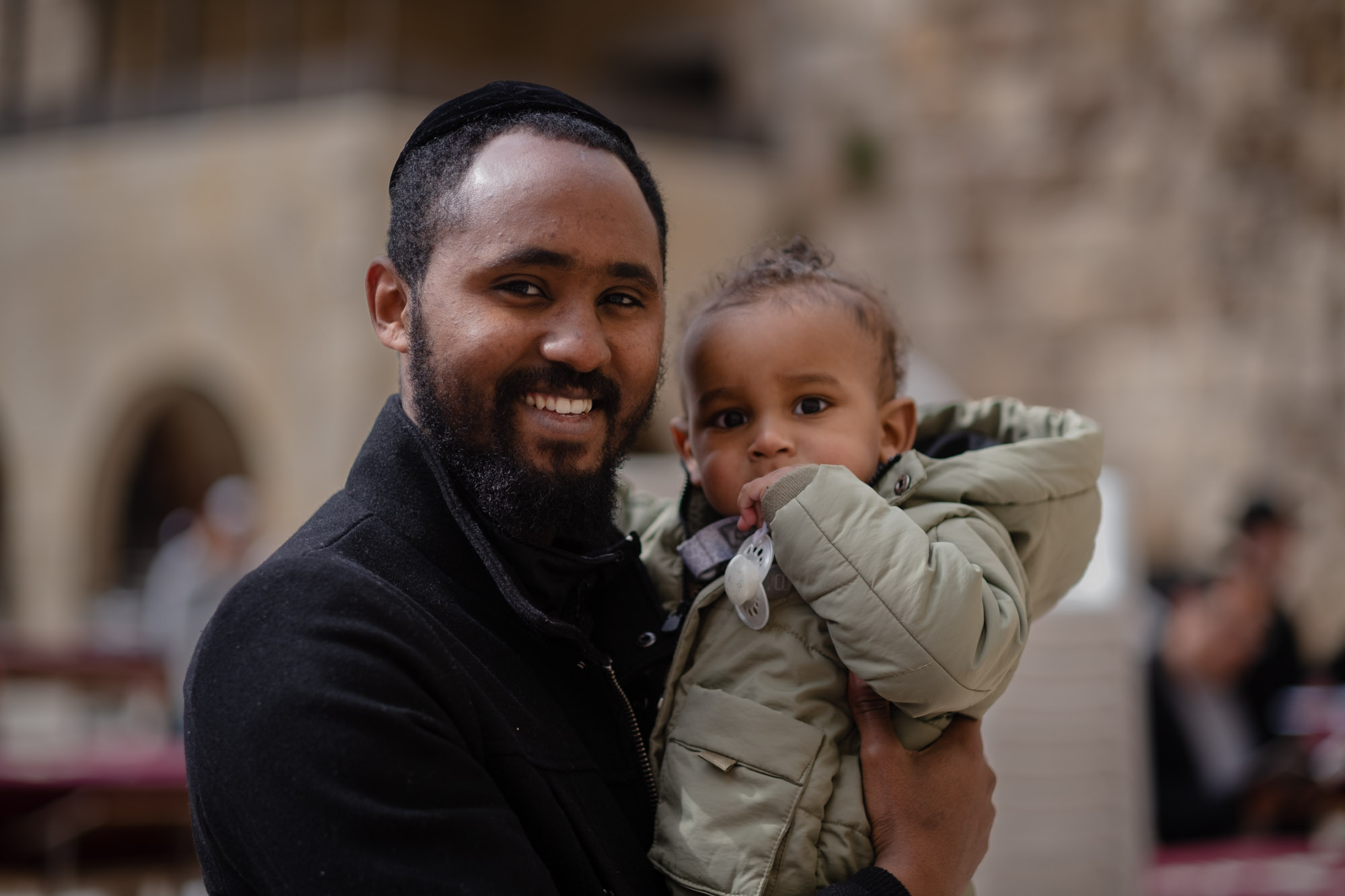 A smiling father holds a small child in a pale green coat.