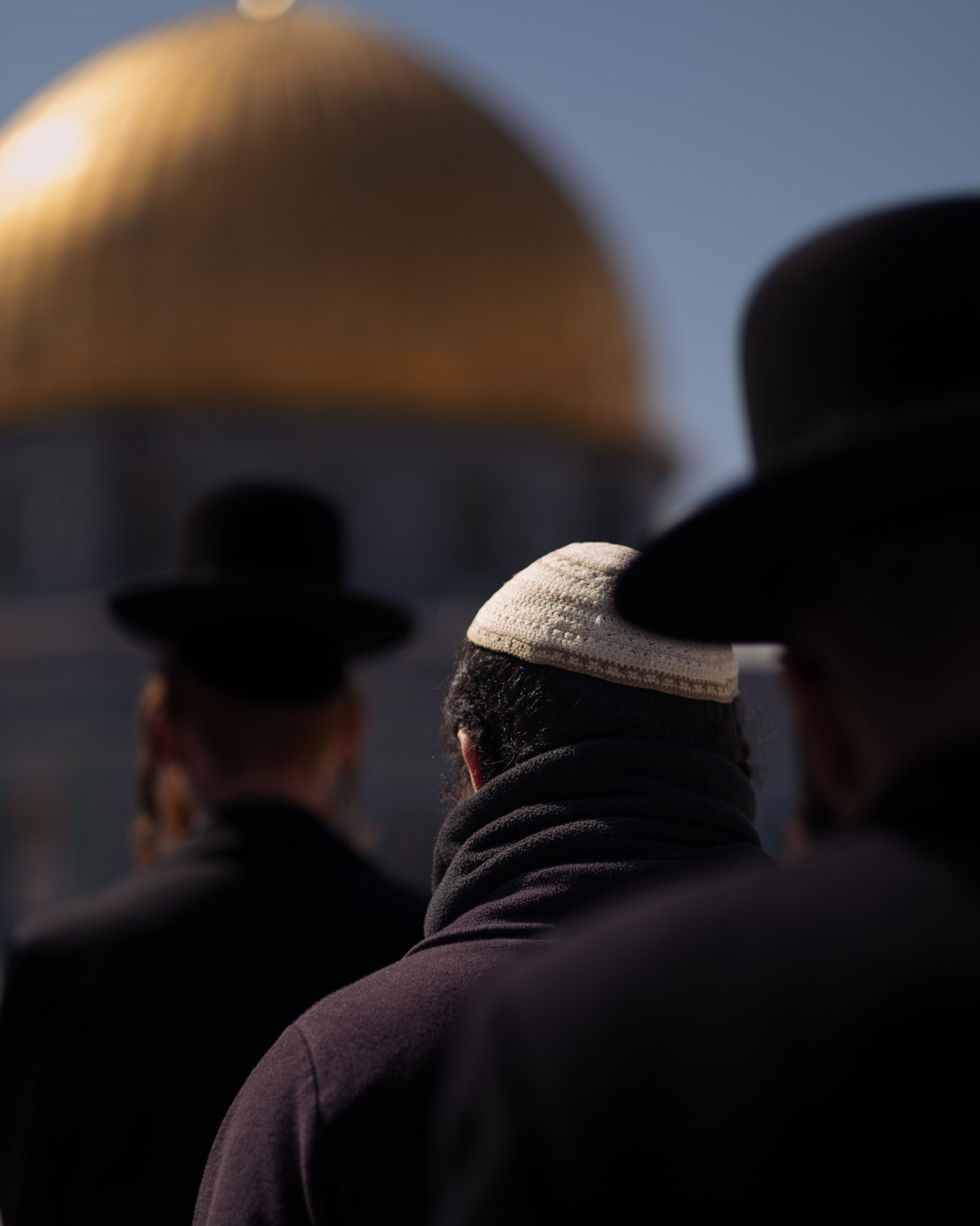 Several people are seen from behind with the Dome of the Rock softly out of focus beyond them.