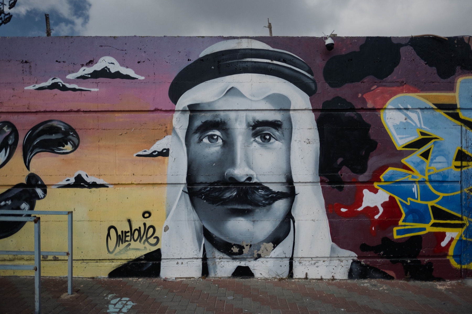 A large public mural depicts a man in traditional Arab clothing against a vivid painted wall.