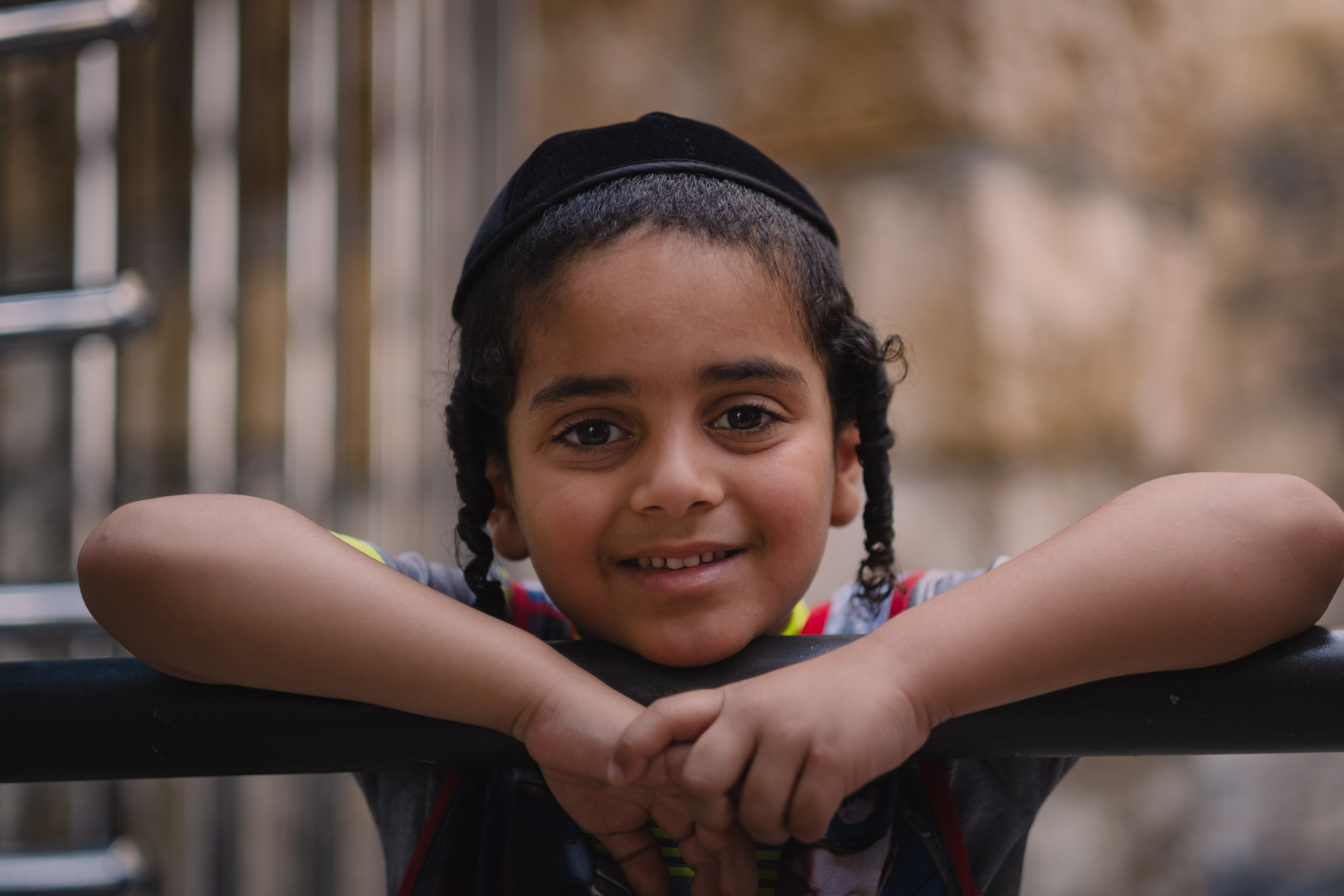 A smiling child leans with both arms across a railing.