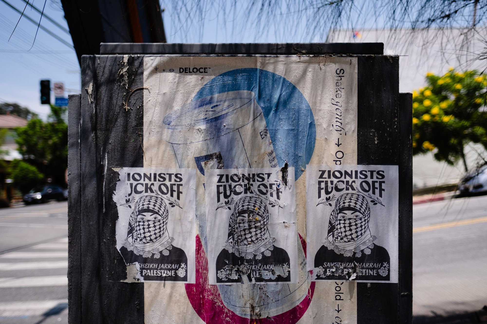 Three weathered political posters are layered across a utility box beside a street.